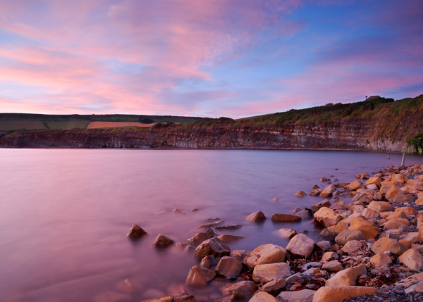 pink sky over calm UK beach rocks and cliffside